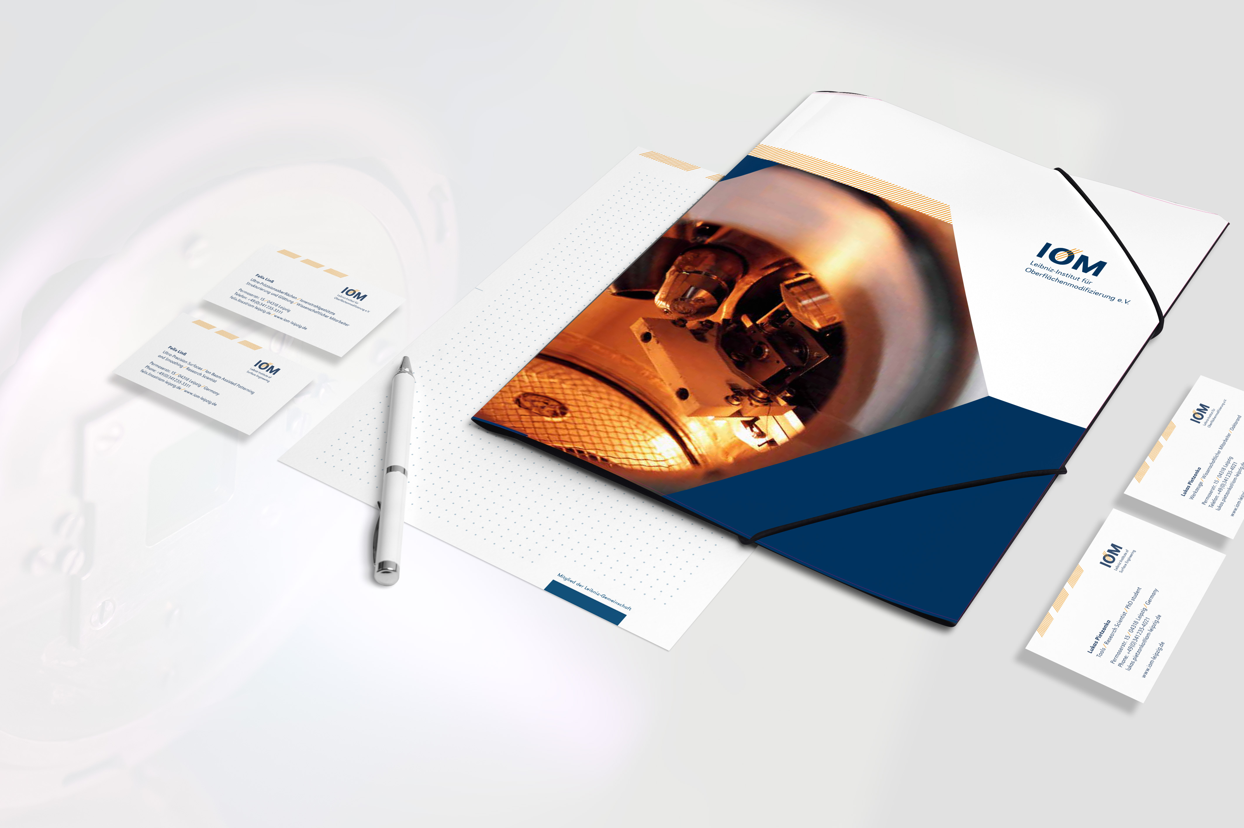 Branding-Materialien des IOM mit Visitenkarten, Mappe und Stift in modernem Design mit weißem Hintergrund und blauen Akzenten.