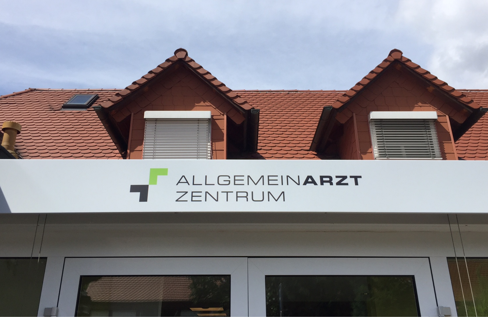 Außenbeschilderung des AllgemeinarztZentrums mit modernem Logo in Grün und Braun auf weißem Hintergrund, gestaltet von Metronom.